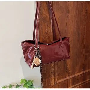 Macro view of burgundy oil-wax leather texture with baseball charms on a flap tote bag