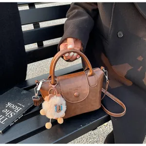 Brown vintage handbag with plush sheep charm and adjustable strap shown on a park bench