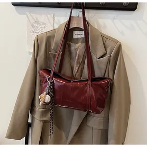 Detail view of burgundy glossy wax leather tote bag with elegant strap and hanging baseball charm