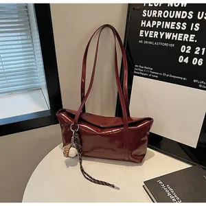 Close-up of deep red glossy leather bag with baseball glove pendant on a white table