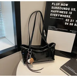 Detail of a black glossy oil wax leather tote bag with long straps and a cute charm