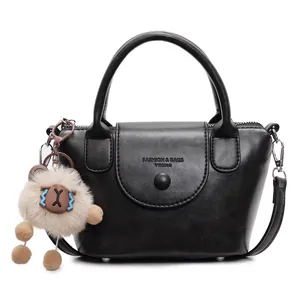 Black matte leather bucket bag with top handle and sheep plush charm on white background