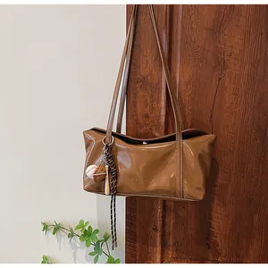 Detail of dark brown glossy leather shoulder bag with clear-k logo and baseball charm