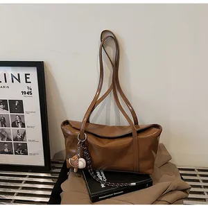 Close-up of caramel wax leather tote bag featuring a baseball and glove charm on long straps