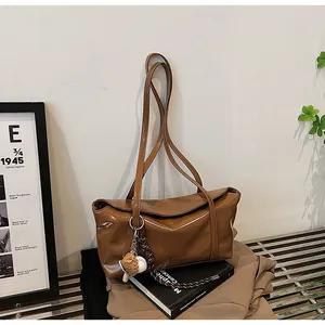 Detailed shot of brown oil-wax leather shoulder bag with a baseball charm and long straps