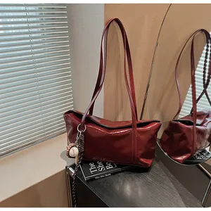 Detail of dark red glossy shoulder bag featuring twin handles and a baseball bag charm