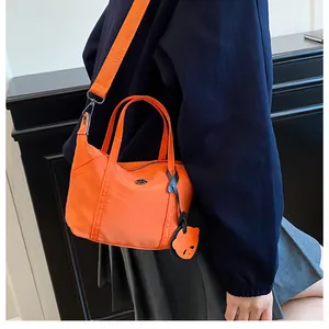 Detail of bright orange nylon crossbody bag with wide shoulder strap and black charm