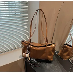 Brown waxed leather shoulder bag with a sporty baseball charm in sunlight