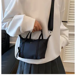 Detail of black nylon mini tote bag with wide crossbody strap and top handle design