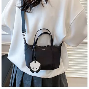 Detail of black nylon tote bag with panda charm and detachable shoulder strap worn by model