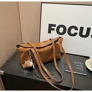 Detail of glossy oil-wax leather shoulder bag in caramel brown with baseball charm pendant