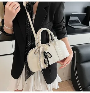 Detalle de bolso de cuero blanco crema con cintas y colgantes decorativos en una modelo