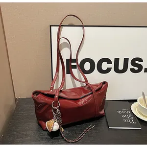 Detail of burgundy glossy leather shoulder bag with baseball charms and woven strap detail