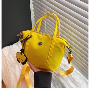 Close-up of bright yellow nylon dumpling bag with metal logo and cute bear charm