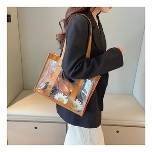 Transparent PVC tote bag with brown trim and canvas strap held by model in studio