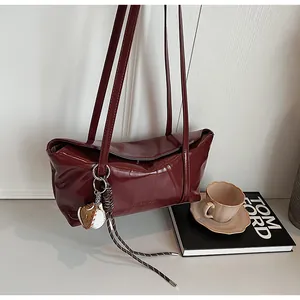 Detailed view of glossy burgundy oil-wax leather texture with logo and charm on a shoulder bag