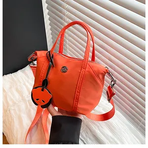 Detail of bright orange crossbody bag with metal M logo and cute panda charm accessory