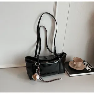 Polished black shoulder bag detail with creative heart and baseball charm on a clean desk