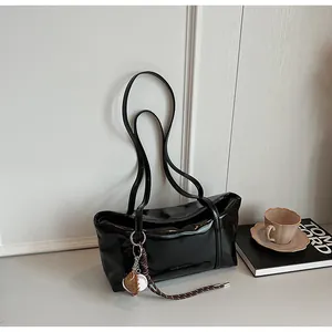 Detail of glossy oil wax leather handbag featuring slim straps and baseball charm