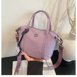 Detail of lavender nylon dumpling bag with top handle, wide strap, and bear charm