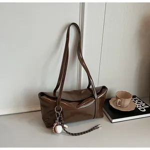 Close-up of brown glossy oil wax leather shoulder bag with a mini baseball charm detail