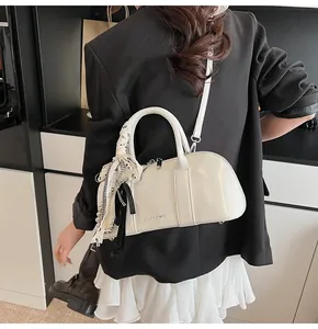 Detalle del bolso cilíndrico beige con elegante pañuelo de cuadros en el asa