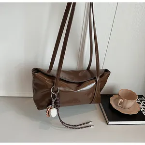 Detail of dark brown oil wax leather shoulder bag with chic baseball glove charm