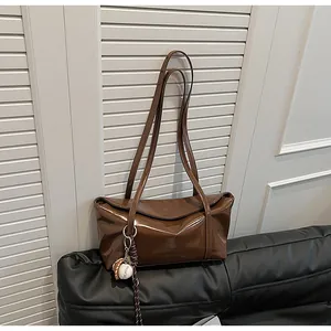 Detail view of glossy brown wax leather shoulder bag with a unique baseball keychain charm