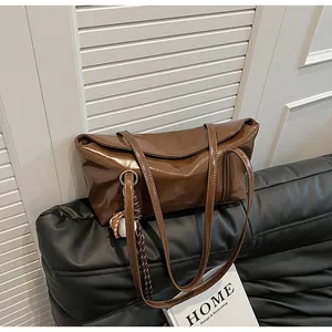 Close-up of brown glossy oil wax leather tote bag with stylish charm on leather sofa