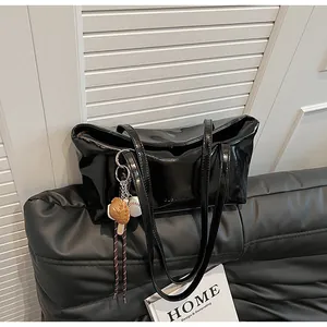 Detail of glossy black wax leather tote bag with long shoulder straps and sports charms