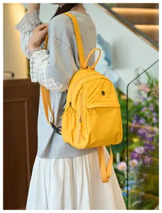 Detail view of yellow nylon backpack featuring side pockets and adjustable straps on model