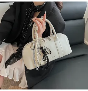 Detalle de bolso Boston en cuero blanco con dijes de cinta y cremallera metálica