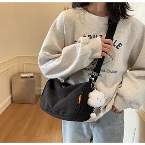 Detail of black corduroy messenger bag with orange label and white cloud charm on model