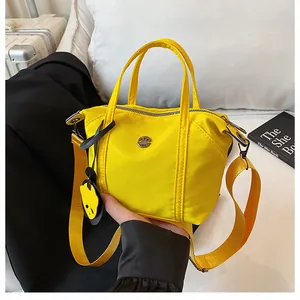 Detail of bright yellow nylon dumpling bag with metal logo and cute smiley pendant