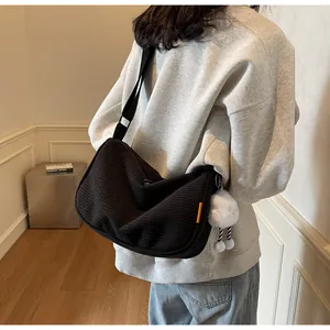 Detail of black corduroy crossbody bag with adjustable strap and plush pendant accessory