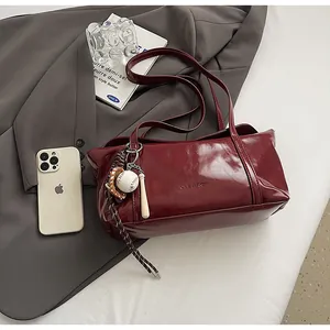 Macro shot of dark red glossy leather tote with baseball charm on a grey blazer