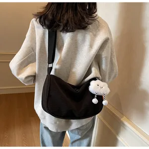 Rear view of model wearing a black corduroy hobo bag with a white plush cloud charm