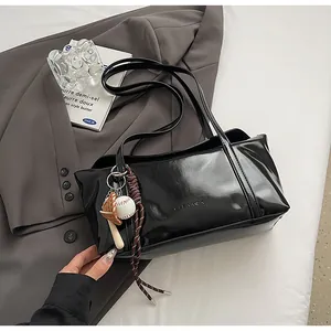 Detail of black glossy shoulder bag with baseball charms on a grey blazer backdrop