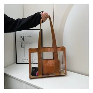 Transparent PVC tote bag featuring brown straps and matching inner pouch on a white pedestal