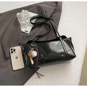 Detail view of a black glossy patent leather shoulder bag with stylish baseball charms