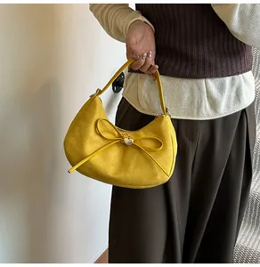 Detail van gele suède hobo tas met lederen strik en gouden hartvormige hanger