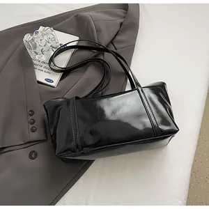 Detail of glossy oil wax leather black tote bag resting on a grey blazer in a studio setting