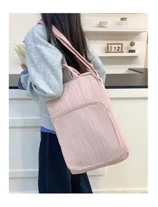 Pink pleated nylon tote bag with front zipper pocket shown on a model's shoulder