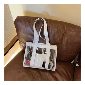 Detail shot of a transparent PVC tote bag with white nylon straps on a vintage leather sofa