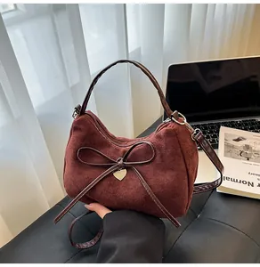 Detailweergave van bordeauxrode suède handtas met decoratieve strik en gouden hartje