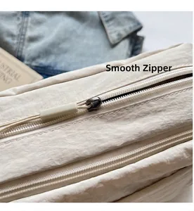 Close-up of smooth metal zipper and nylon texture on minimalist cream crossbody bag