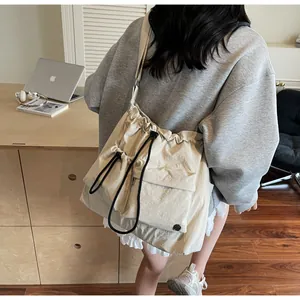 Detail view of beige nylon crossbody bag featuring drawstring pockets and round metal logo