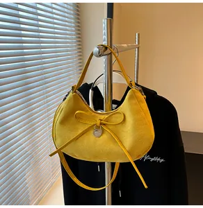 Detail van gele suède halve maan tas met strik en hartvormige metalen hanger aan de tas