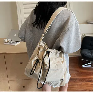 Detail of a large beige nylon crossbody bag featuring adjustable drawstrings and wide strap