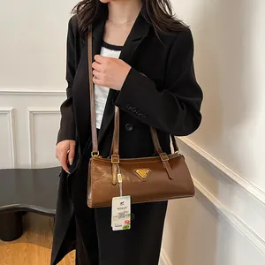 Braune Baguette-Schultertasche aus Lackleder mit goldenem Logo vor weißem Hintergrund